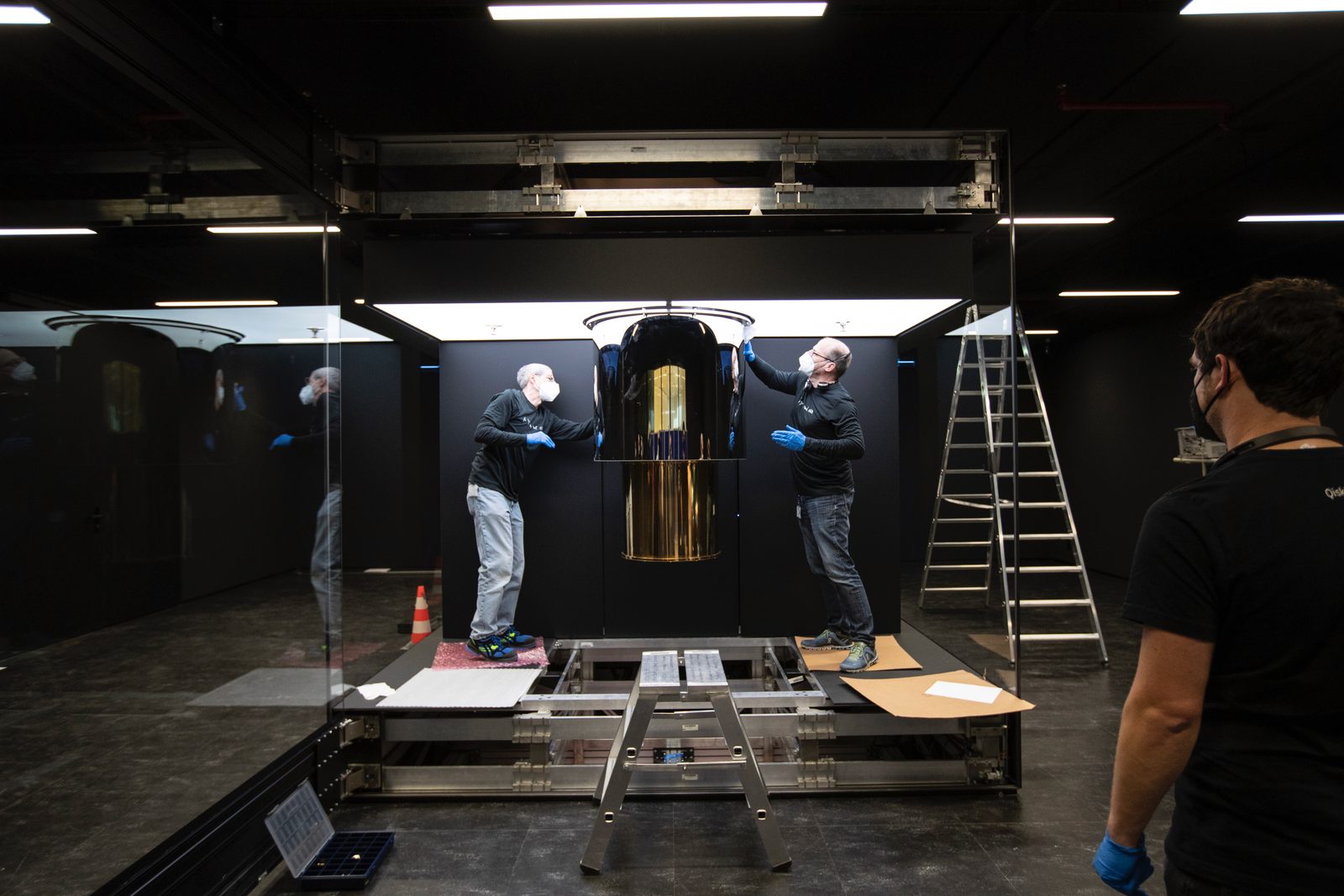 An IBM Q System One quantum computer enclosed in its glass cube, with the gold-plated dilution refrigerator suspended inside.
